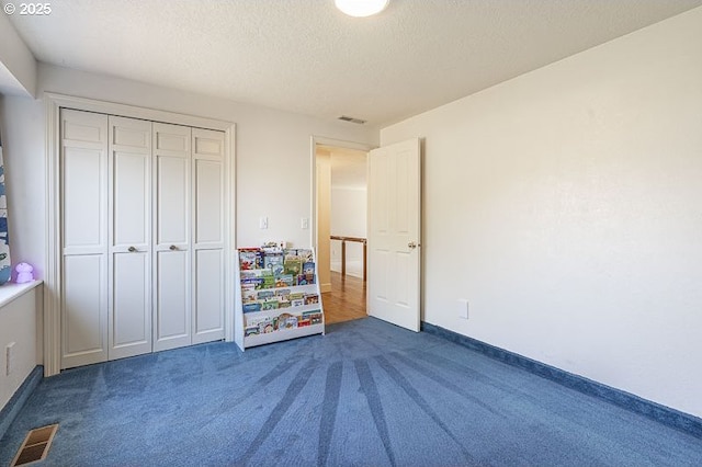 unfurnished bedroom with dark colored carpet, a textured ceiling, visible vents, and a closet