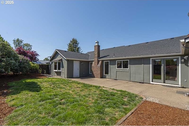 rear view of property with a lawn, a shingled roof, a patio area, and a chimney