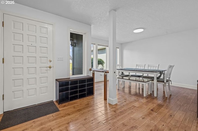 dining space with baseboards, light wood-type flooring, and a textured ceiling