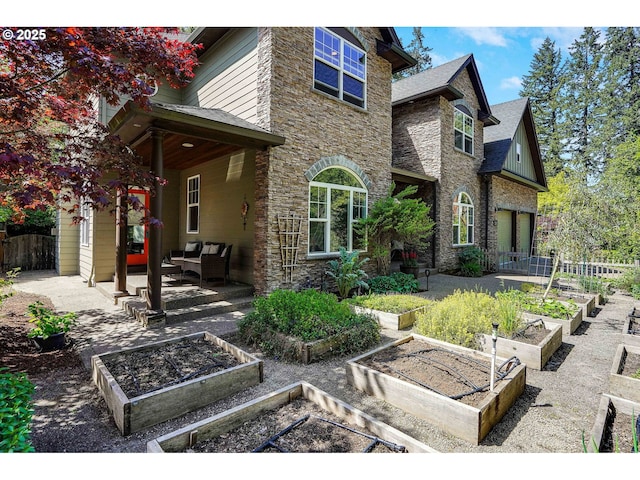 rear view of house featuring fence, a patio, a vegetable garden, and stone siding