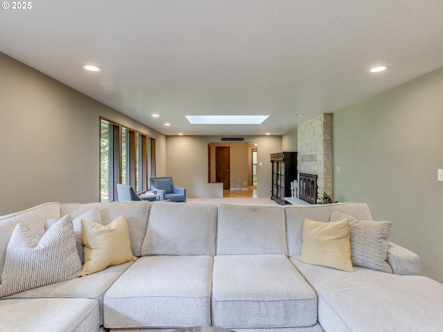 living room featuring a stone fireplace, recessed lighting, and a skylight
