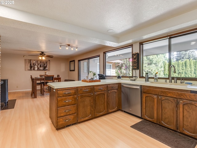 kitchen with a sink, light wood-style flooring, a peninsula, and dishwasher
