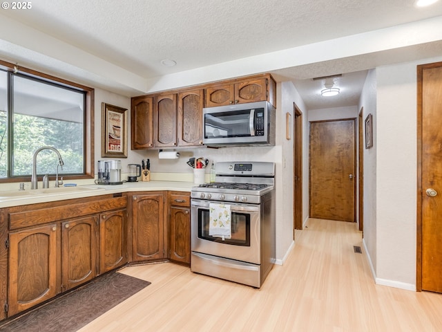 kitchen featuring appliances with stainless steel finishes, a sink, light countertops, a textured ceiling, and light wood-style flooring
