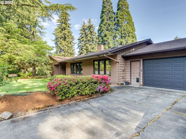 single story home with a front lawn, a chimney, brick siding, an attached garage, and driveway