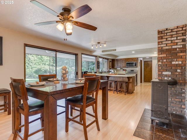 dining space featuring light wood-style floors, a ceiling fan, a wood stove, and a textured ceiling
