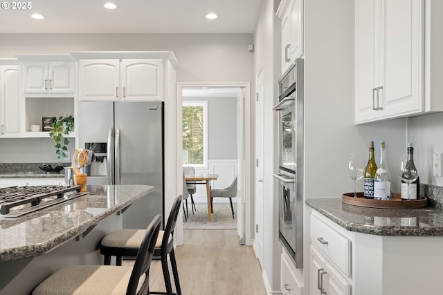 10695 SW Meier Dr, Tualatin, OR 97062 - kitchen with white cabinetry, dark stone counters, a kitchen breakfast bar, appliances with stainless steel finishes, and light wood-type flooring