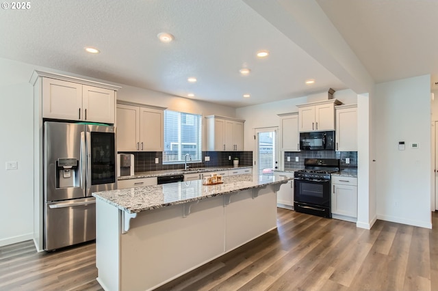 1319 S 29th Blvd, Cornelius, OR 97113 - kitchen featuring black appliances, a sink, backsplash, a kitchen bar, and light stone counters
