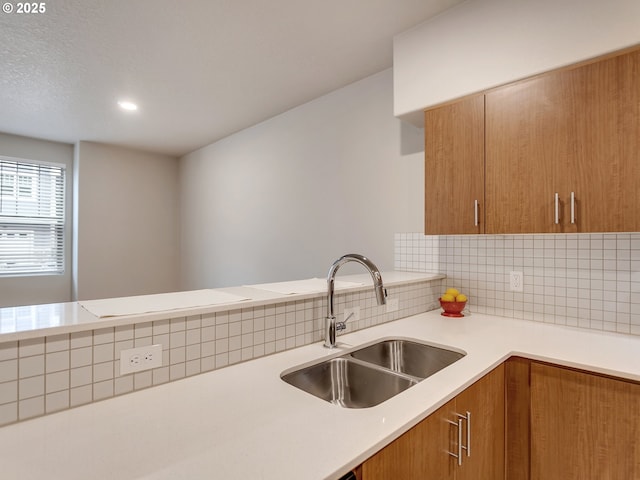 kitchen with brown cabinets, tasteful backsplash, light countertops, a sink, and a peninsula