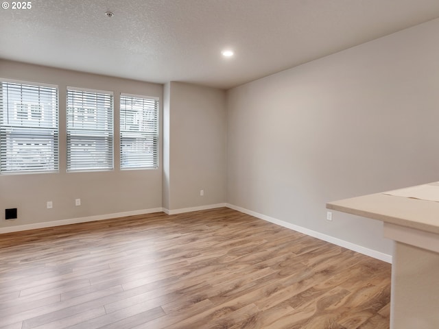 unfurnished room with a textured ceiling, recessed lighting, light wood-style flooring, and baseboards