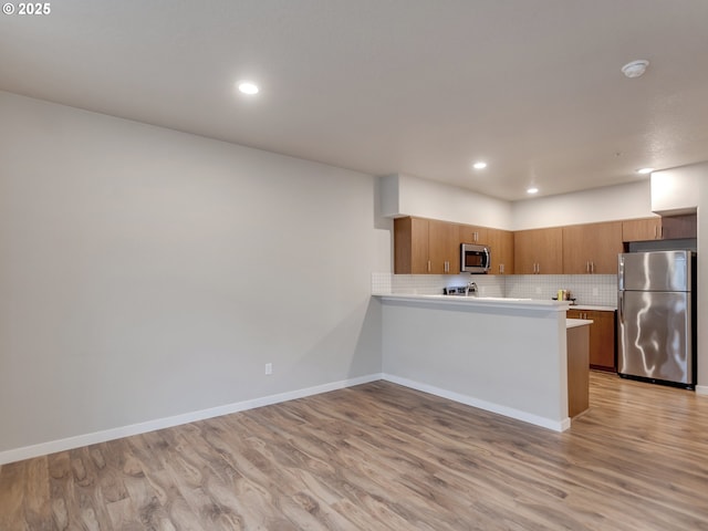 kitchen featuring light countertops, appliances with stainless steel finishes, light wood-type flooring, brown cabinets, and decorative backsplash