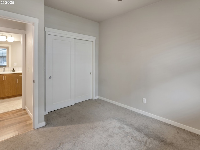 unfurnished bedroom with a closet, baseboards, a sink, and light colored carpet