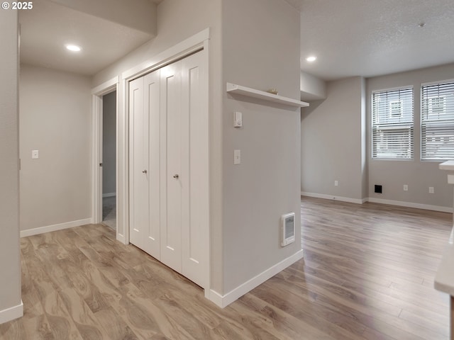 hallway featuring light wood finished floors, baseboards, visible vents, and recessed lighting