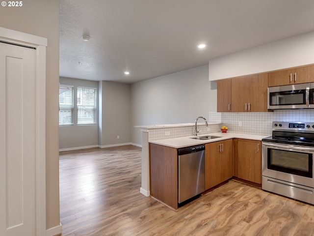 kitchen featuring brown cabinets, tasteful backsplash, appliances with stainless steel finishes, a sink, and a peninsula