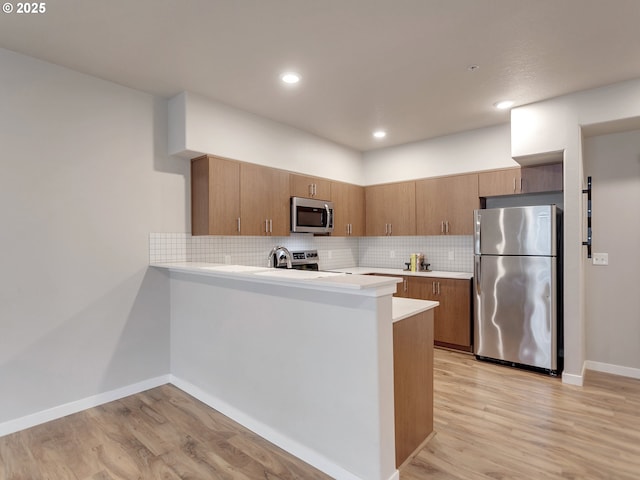 kitchen with brown cabinets, stainless steel appliances, light countertops, backsplash, and light wood-style floors