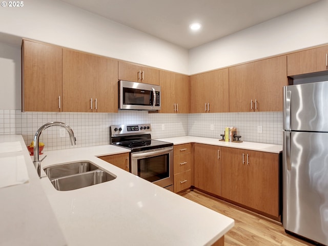 kitchen featuring light wood-style flooring, a sink, stainless steel appliances, light countertops, and backsplash