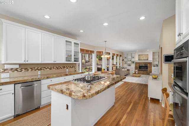 kitchen featuring stainless steel appliances, a kitchen island, a glass covered fireplace, and white cabinets