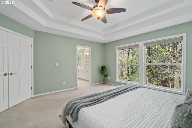 bedroom featuring connected bathroom, ceiling fan, baseboards, light carpet, and a raised ceiling