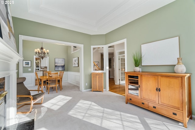 living area with a wainscoted wall, ornamental molding, a raised ceiling, a decorative wall, and a chandelier