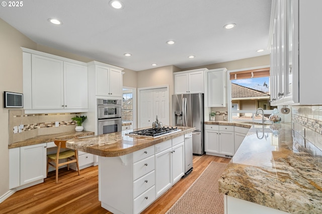 kitchen featuring light wood-style flooring, a sink, a kitchen island, stainless steel appliances, and white cabinets