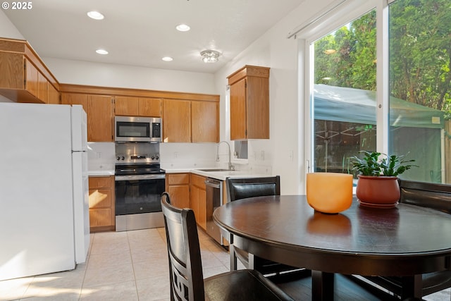 kitchen with light tile patterned flooring, a sink, light countertops, brown cabinetry, and stainless steel appliances