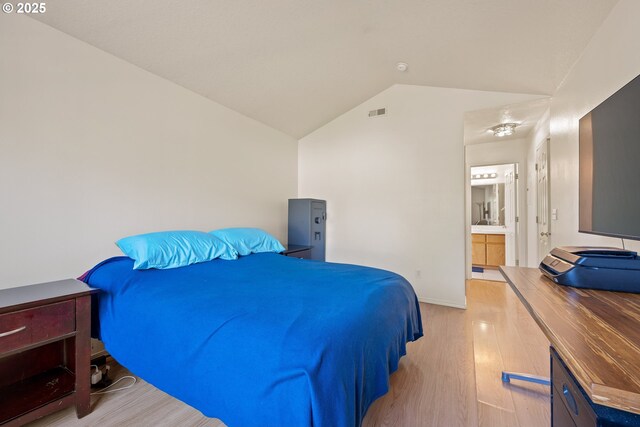 bedroom with connected bathroom, baseboards, wood finished floors, lofted ceiling, and visible vents
