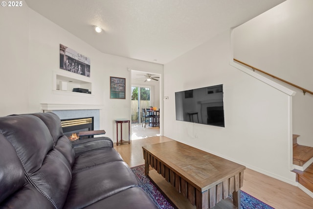 living area featuring stairs, wood finished floors, baseboards, a tiled fireplace, and a ceiling fan