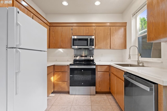 kitchen with brown cabinetry, recessed lighting, a sink, light tile patterned floors, and stainless steel appliances
