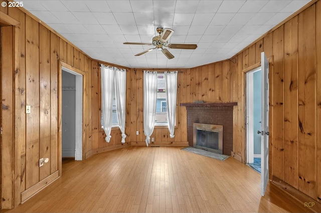 unfurnished living room with a fireplace, light wood finished floors, a ceiling fan, wood walls, and baseboards