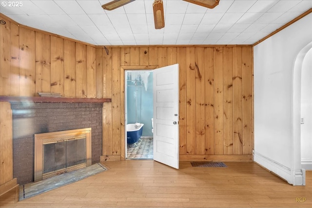 unfurnished living room featuring ceiling fan, a fireplace, baseboards, light wood-style floors, and crown molding