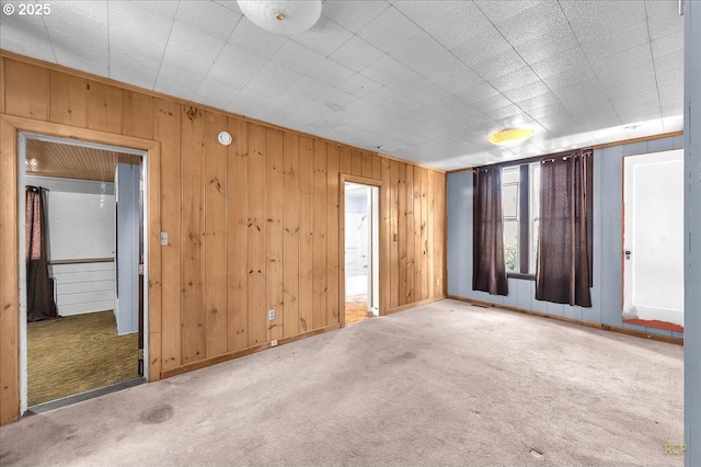 empty room featuring carpet flooring, wooden walls, and baseboards