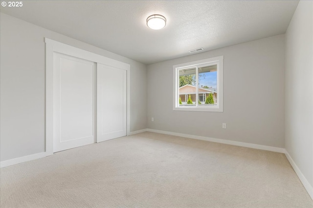 unfurnished bedroom featuring visible vents, baseboards, a closet, and light carpet