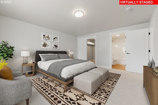 bedroom featuring a walk in closet, ensuite bathroom, and carpet flooring