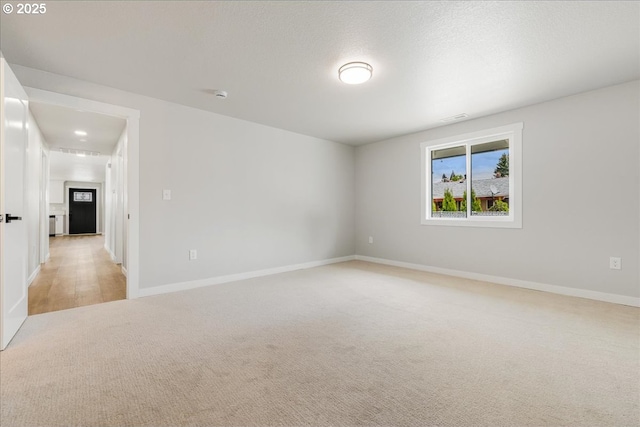 spare room with baseboards and light colored carpet