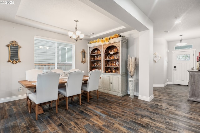 dining room with dark hardwood / wood-style flooring, a tray ceiling, a textured ceiling, and a chandelier