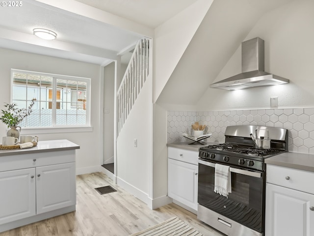 kitchen featuring stainless steel gas stove, white cabinets, wall chimney exhaust hood, and light hardwood / wood-style flooring