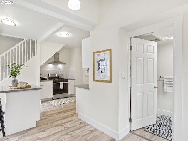 kitchen featuring stainless steel range with gas cooktop, wall chimney range hood, white cabinetry, and light hardwood / wood-style floors