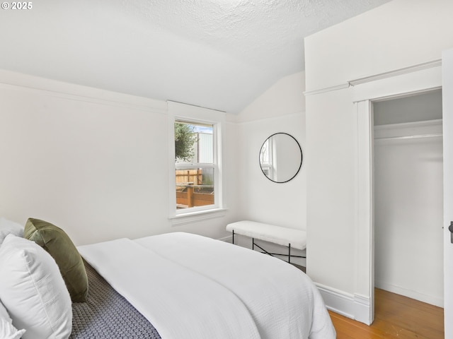 bedroom with light wood-type flooring, a closet, lofted ceiling, and a textured ceiling