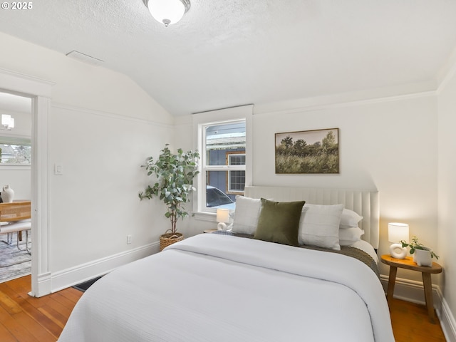 bedroom with vaulted ceiling, wood-type flooring, and a textured ceiling