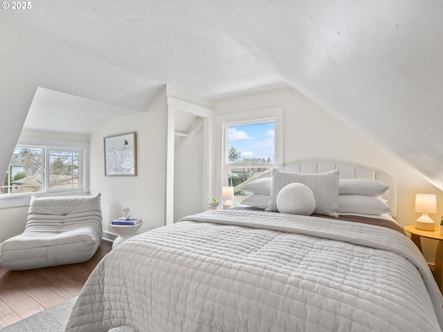 bedroom with hardwood / wood-style floors, multiple windows, lofted ceiling, and a textured ceiling