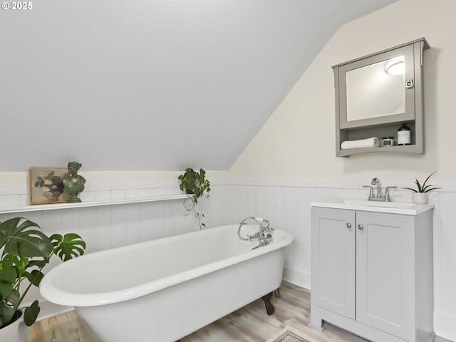 bathroom with vanity, vaulted ceiling, a tub to relax in, and hardwood / wood-style floors