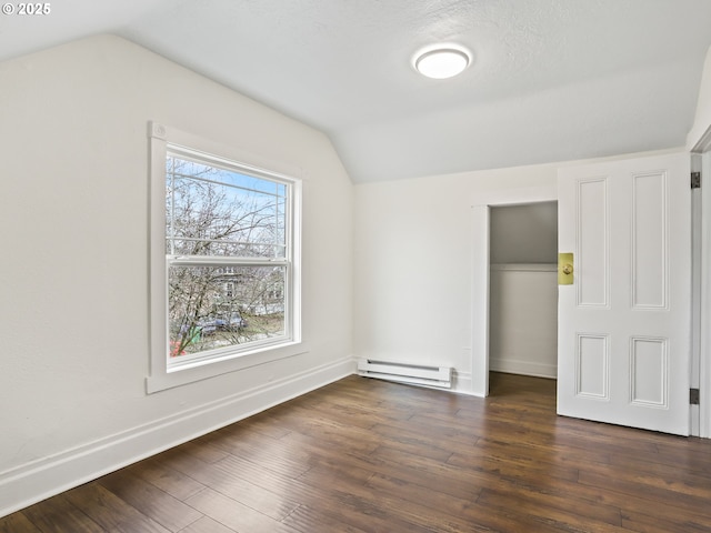 unfurnished bedroom with vaulted ceiling, dark wood-type flooring, a baseboard heating unit, and a closet