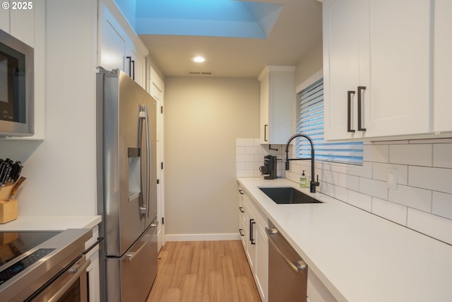 kitchen with light wood-type flooring, decorative backsplash, appliances with stainless steel finishes, white cabinetry, and a sink