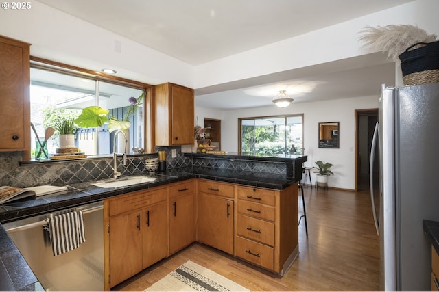 kitchen featuring appliances with stainless steel finishes, a sink, light wood-style floors, and decorative backsplash