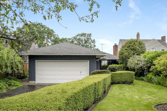 view of front of property featuring a front lawn, a chimney, asphalt driveway, a shingled roof, and an attached garage