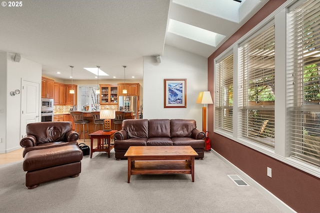 living room with vaulted ceiling with skylight and light colored carpet