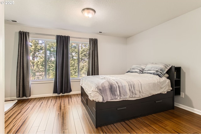 bedroom featuring visible vents, baseboards, a textured ceiling, and wood finished floors