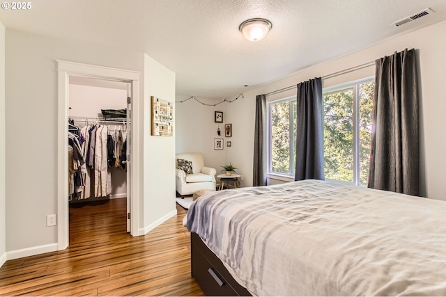 bedroom featuring visible vents, hardwood / wood-style floors, a closet, baseboards, and a spacious closet