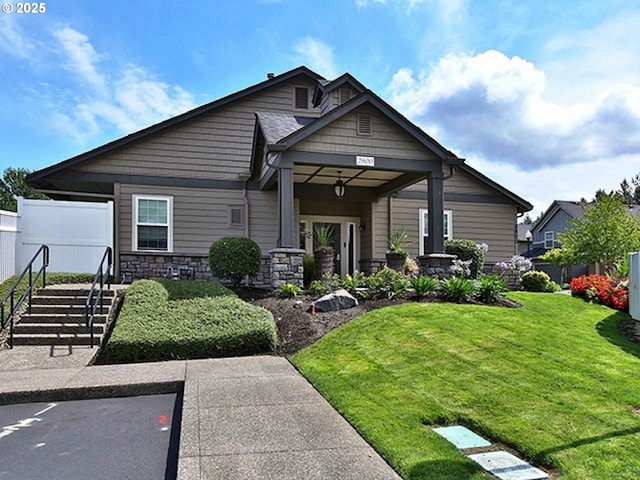 view of front facade featuring stone siding, a front yard, and fence