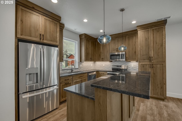 kitchen featuring appliances with stainless steel finishes, tasteful backsplash, brown cabinets, a sink, and light wood-style flooring