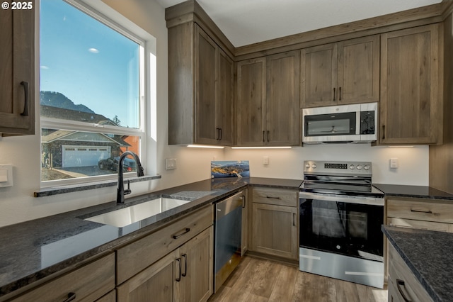 kitchen featuring dark stone counters, stainless steel appliances, a sink, and light wood finished floors